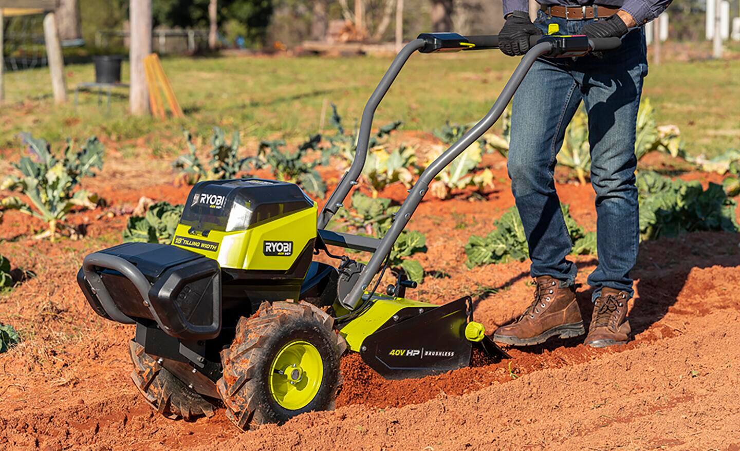 Gardener pushing a tiller through a garden bed