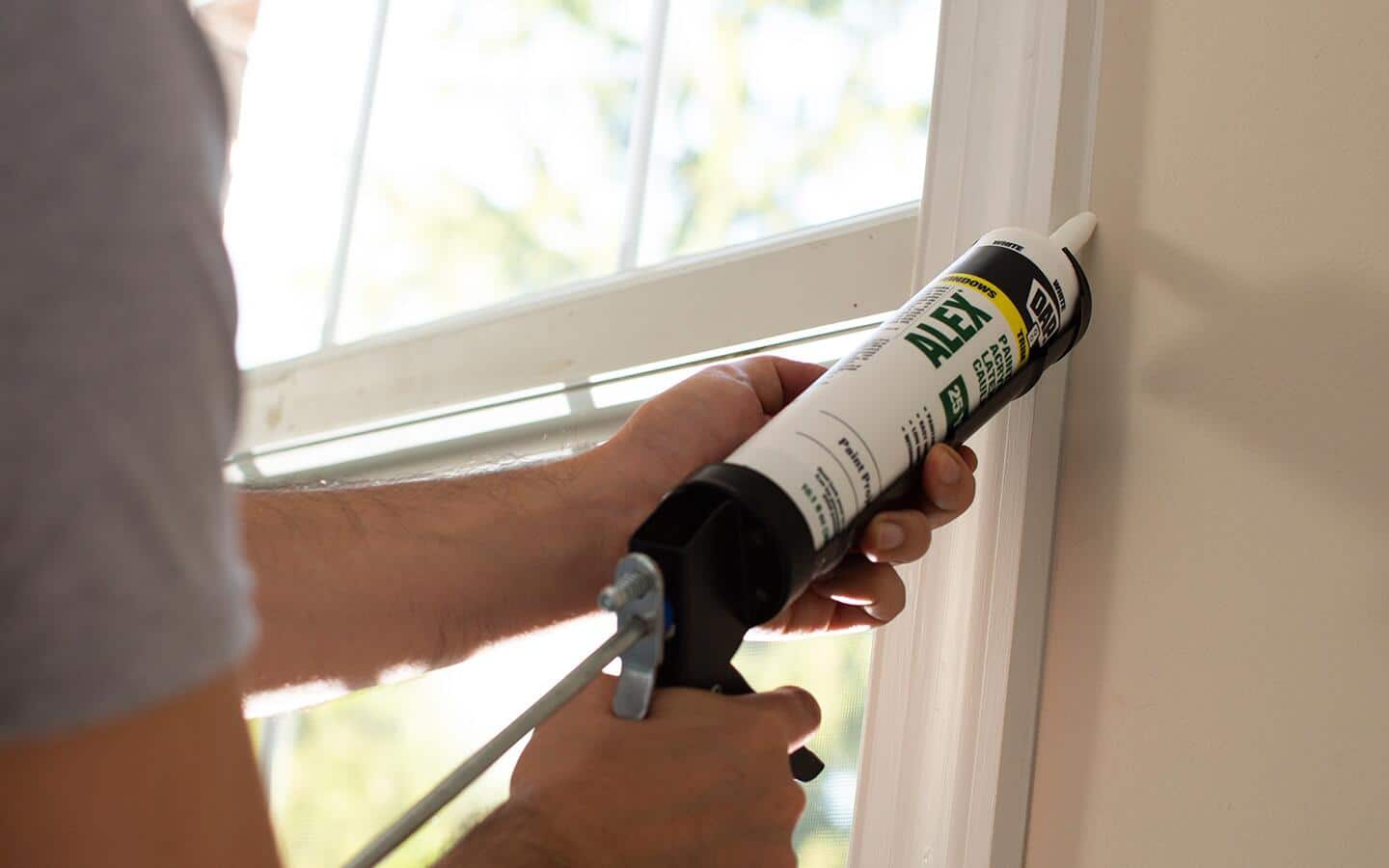 Person sealing a window with caulk Person sealing a window with caulk