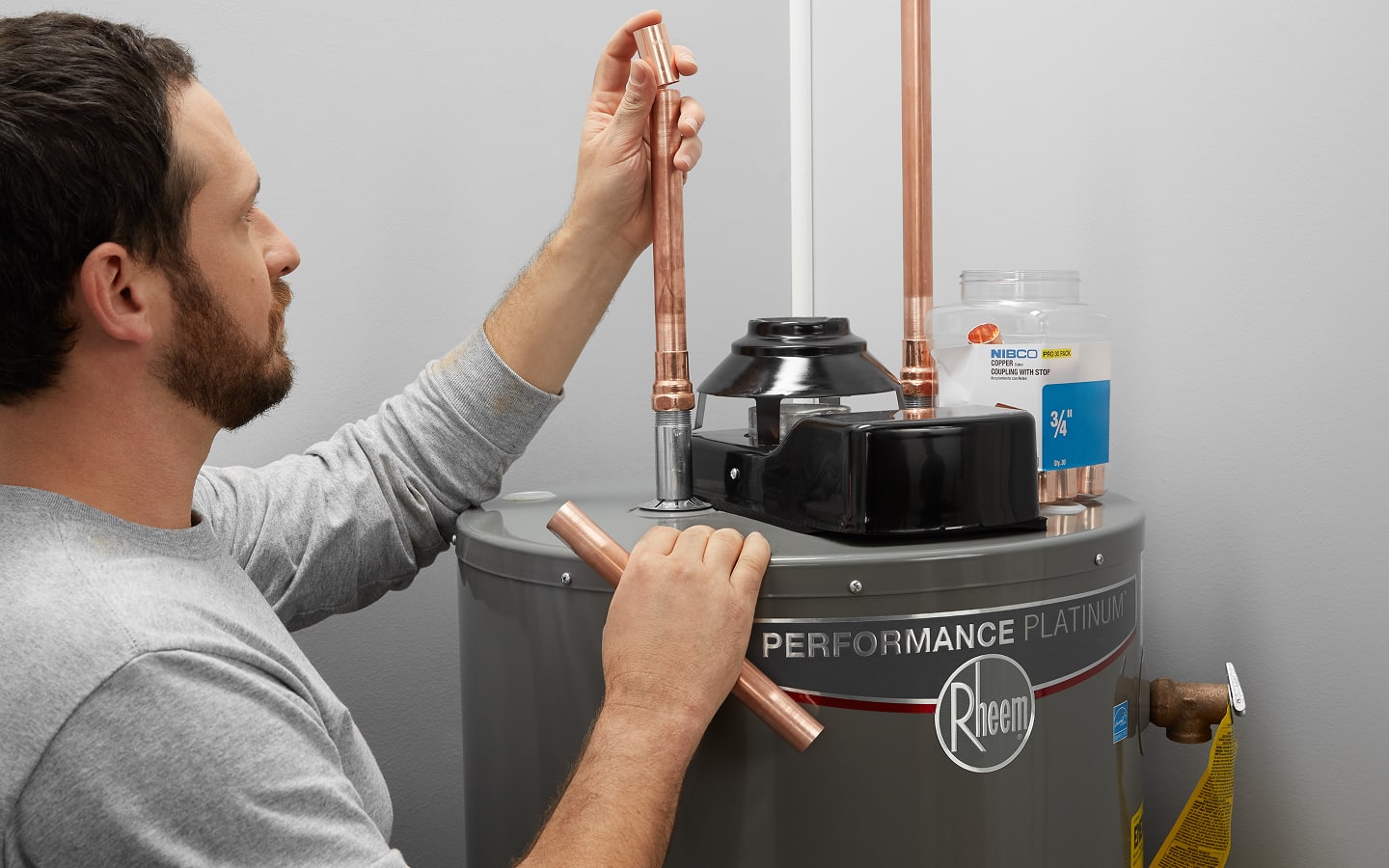 A plumber installs a water line at a water heater.