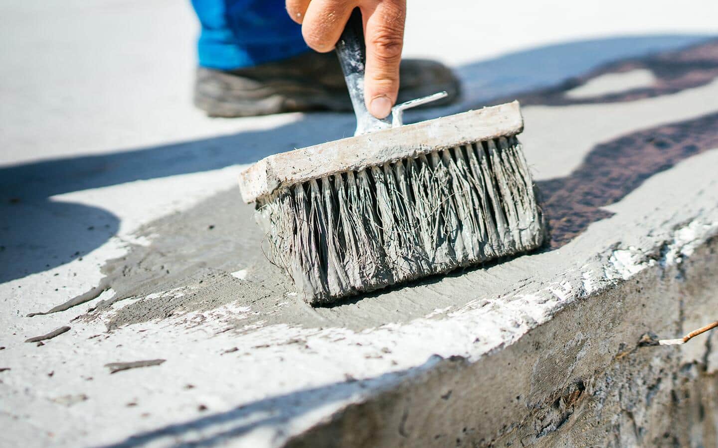 A person uses a brush to finish a wet concrete surface. A person uses a brush to finish a wet concrete surface.
