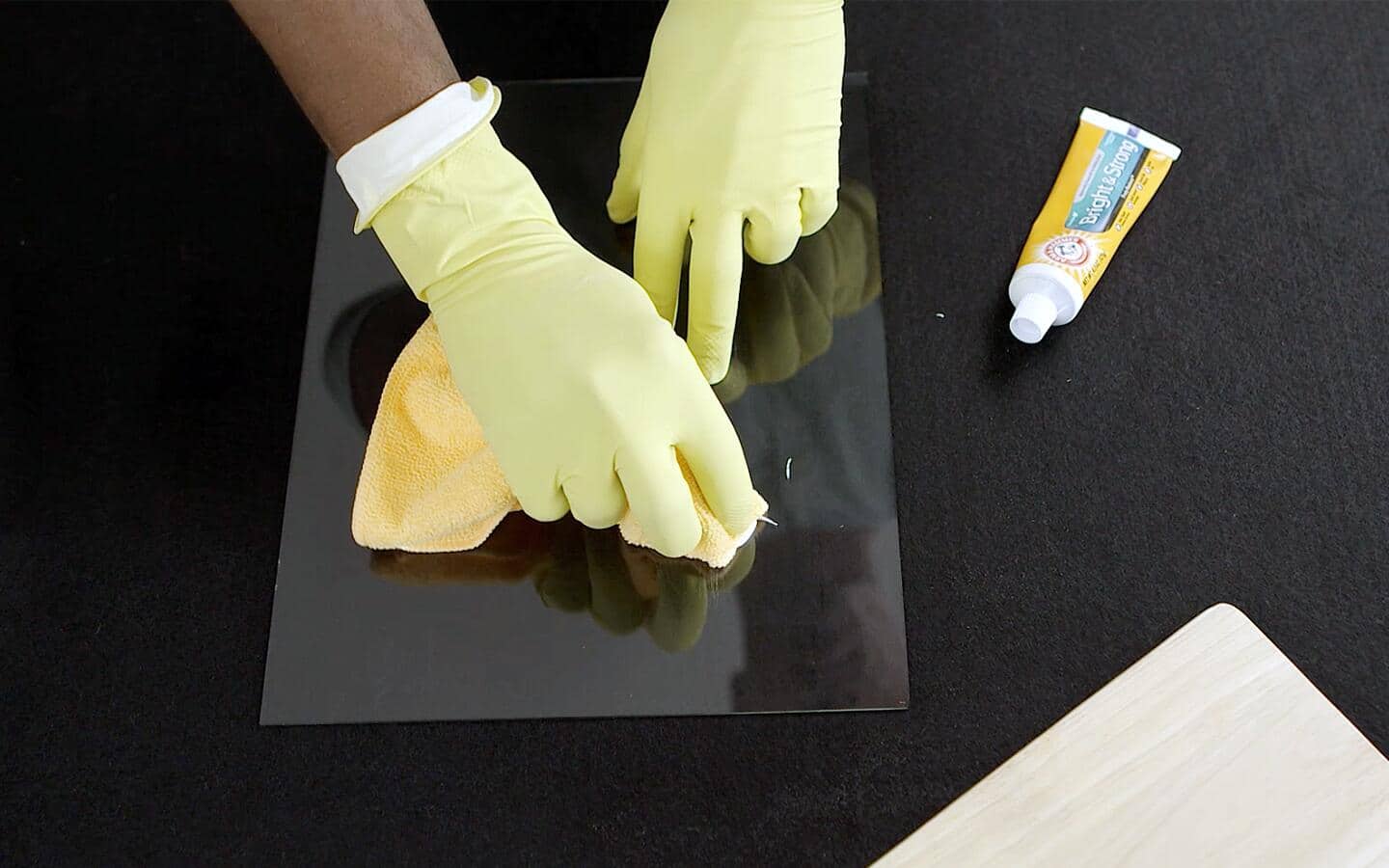 A gloved individual rubs a cloth with toothpaste to buff away glass scratches.