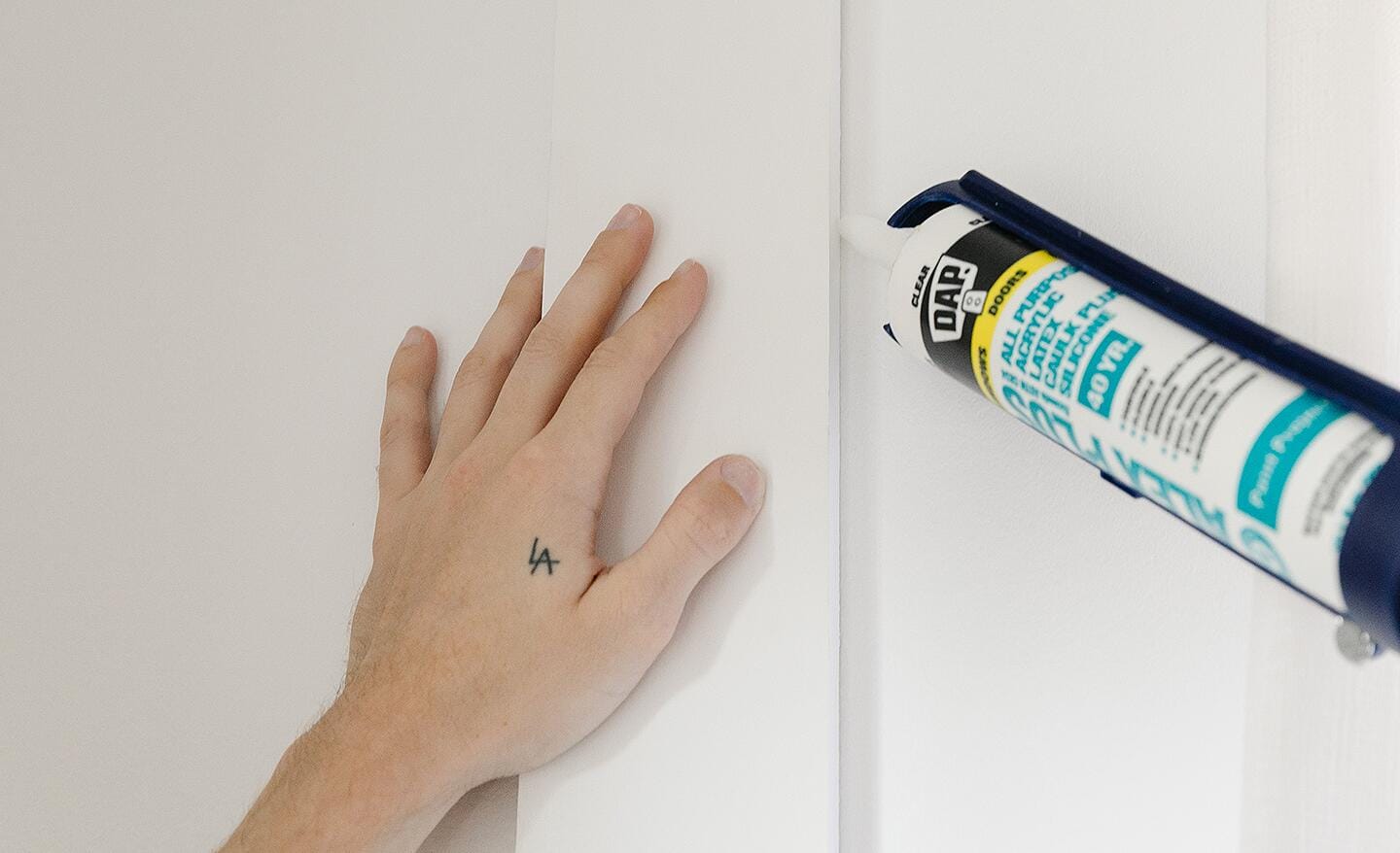 A person caulking the edges of a vertical wall board.