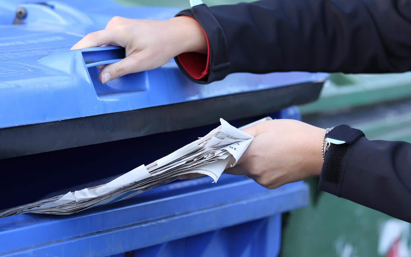 A person recycling old newspapers in a blue bin. A person recycling old newspapers in a blue bin.