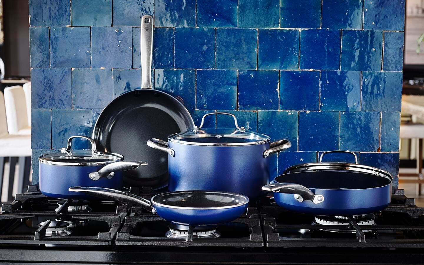 A blue cookware set with two skillets and a stock pot sitting on a stovetop.