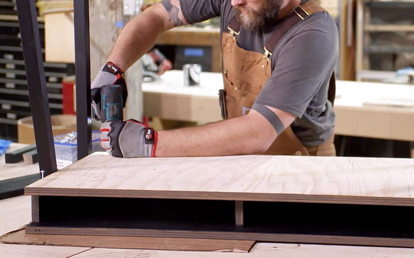 A person in a work apron permanently assembling DIY desk parts.  
