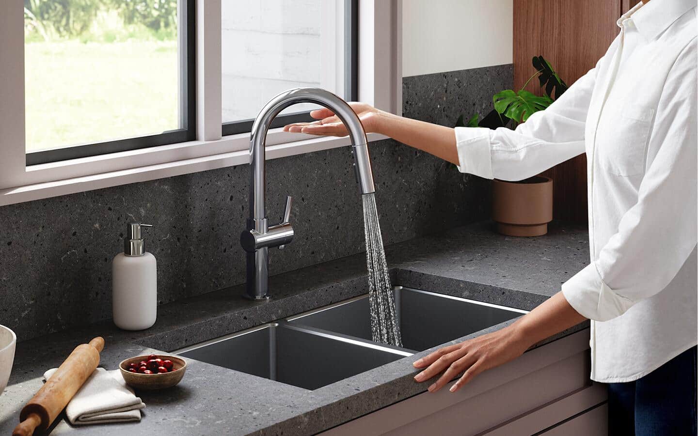 A person running a kitchen faucet in a double sink to test for water leaks. A person running a kitchen faucet in a double sink to test for water leaks.