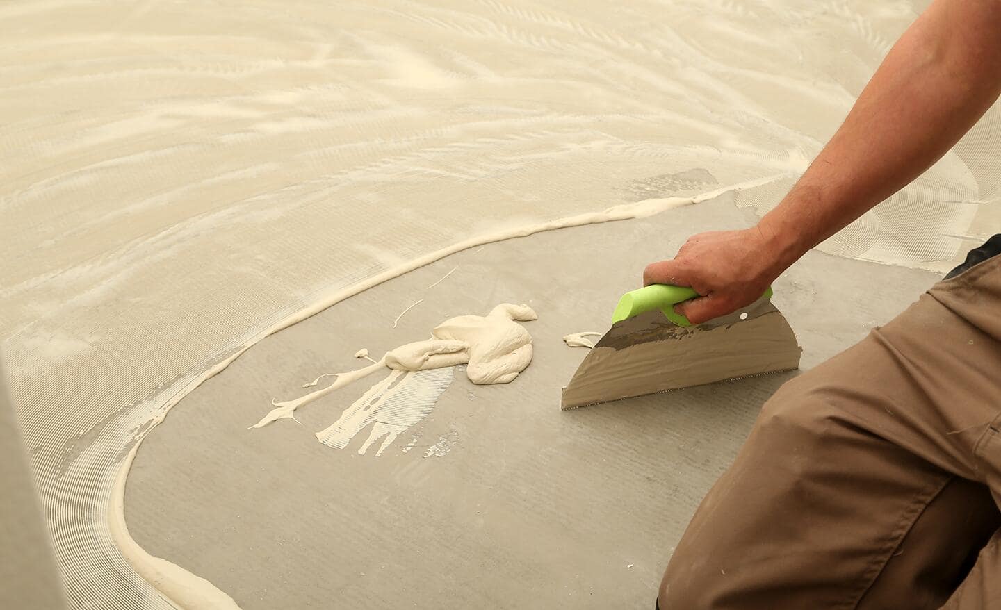 A person uses a trowel to spread vinyl adhesive on concrete floor.