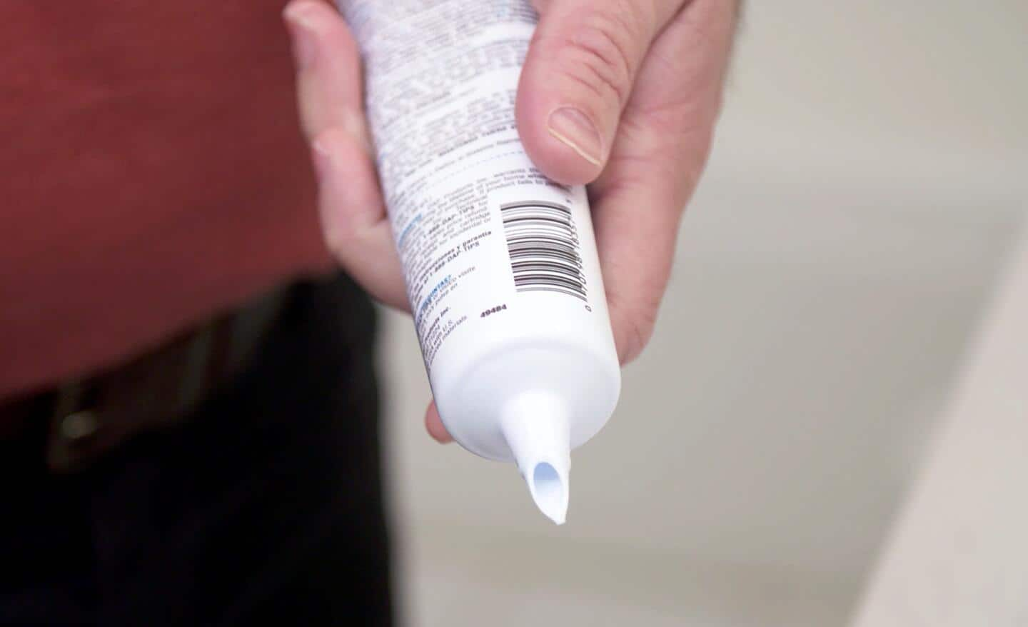 A person holds an opened caulk tube before sealing it for storage.