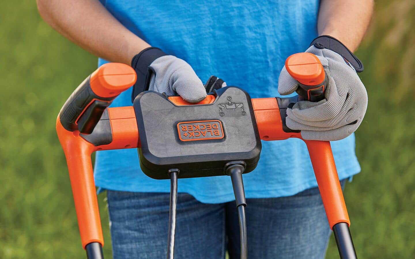 Someone in work gloves adjusting the handles of an orange push power mower. Someone in work gloves adjusting the handles of an orange push power mower.