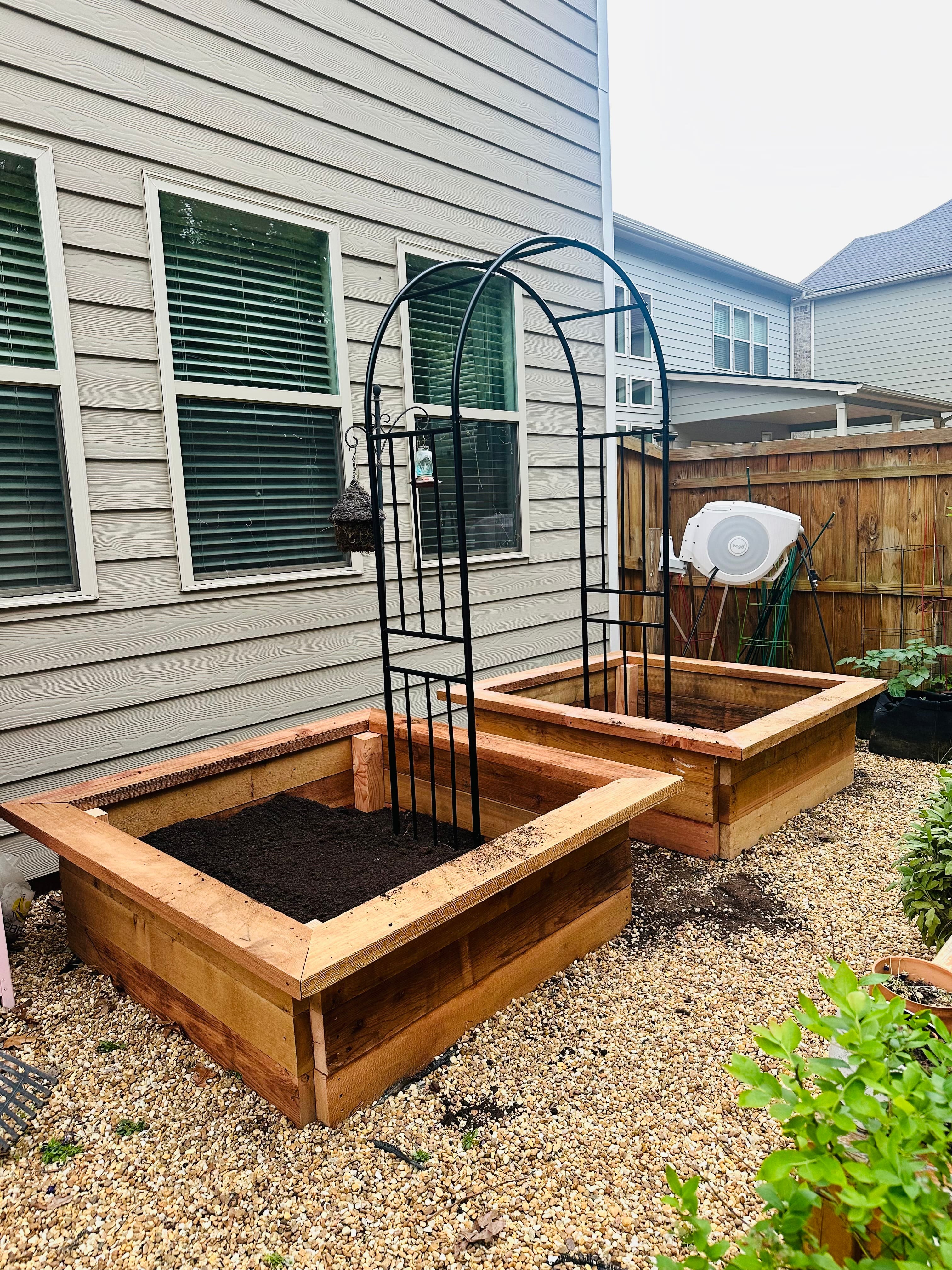An in-progress shot of two wooden raised garden beds connected by a trellis sitting over a once barren garden space. An in-progress shot of two wooden raised garden beds connected by a trellis sitting over a once barren garden space.