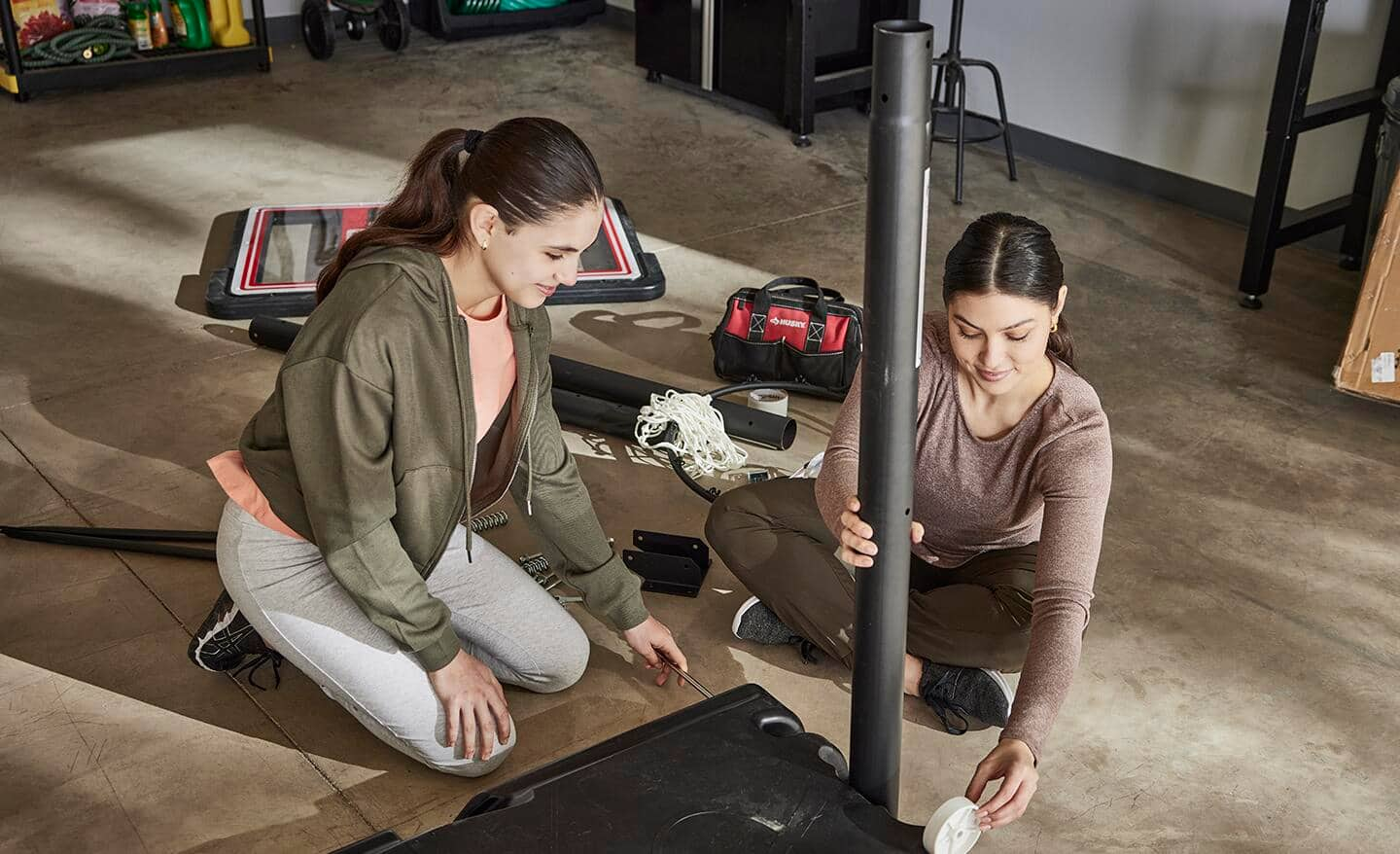 Mom and daughter add the pole and wheel to base of a portable hoop.