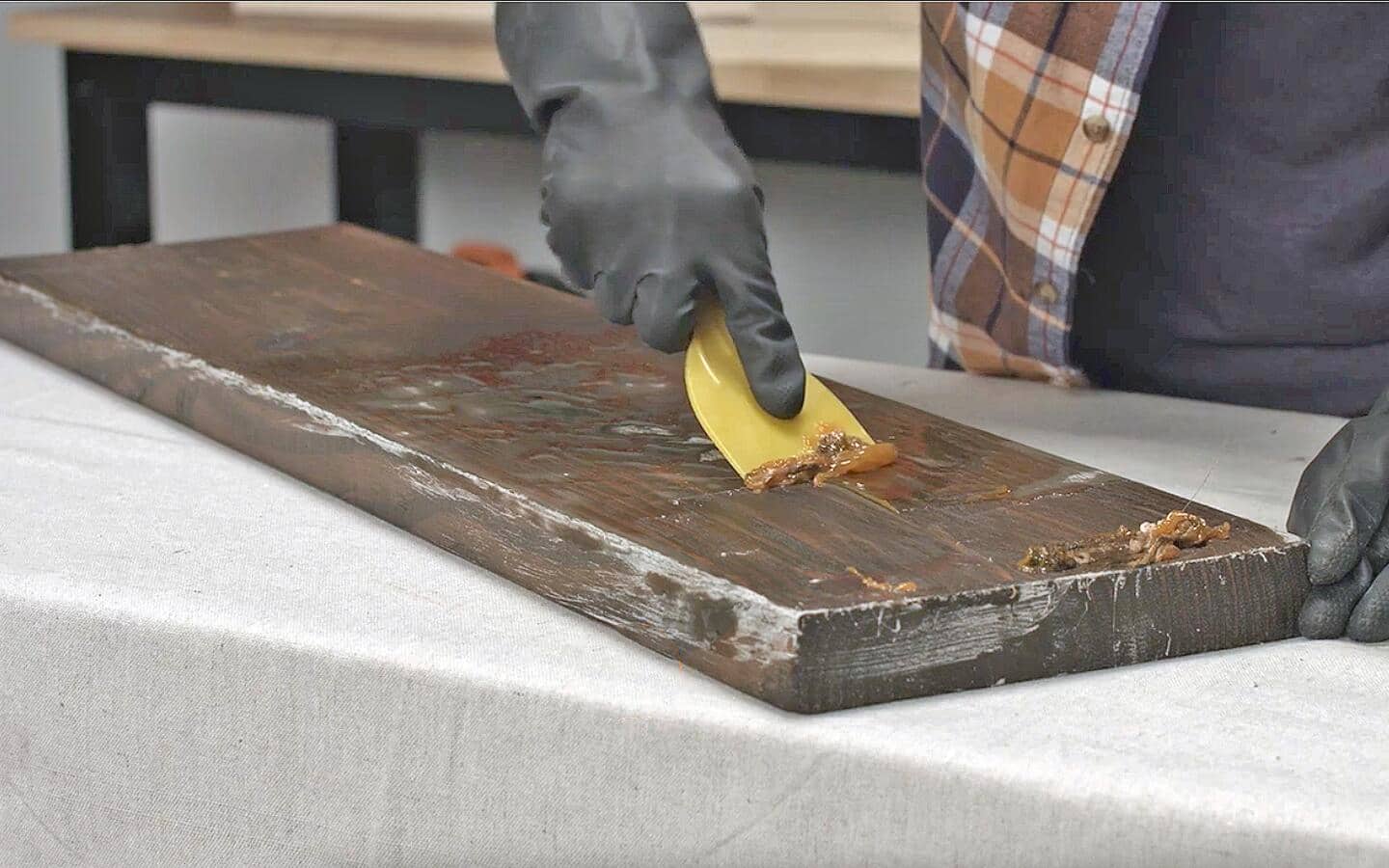A person wearing gloves scrapes a wood board.