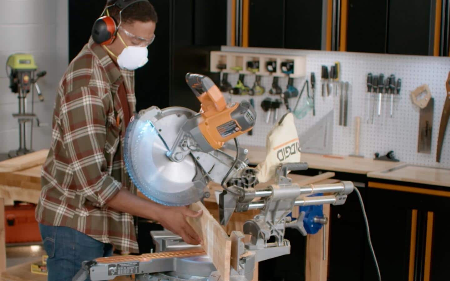 Someone in a brown checkered shirt cuts a wooden board with a miter saw.