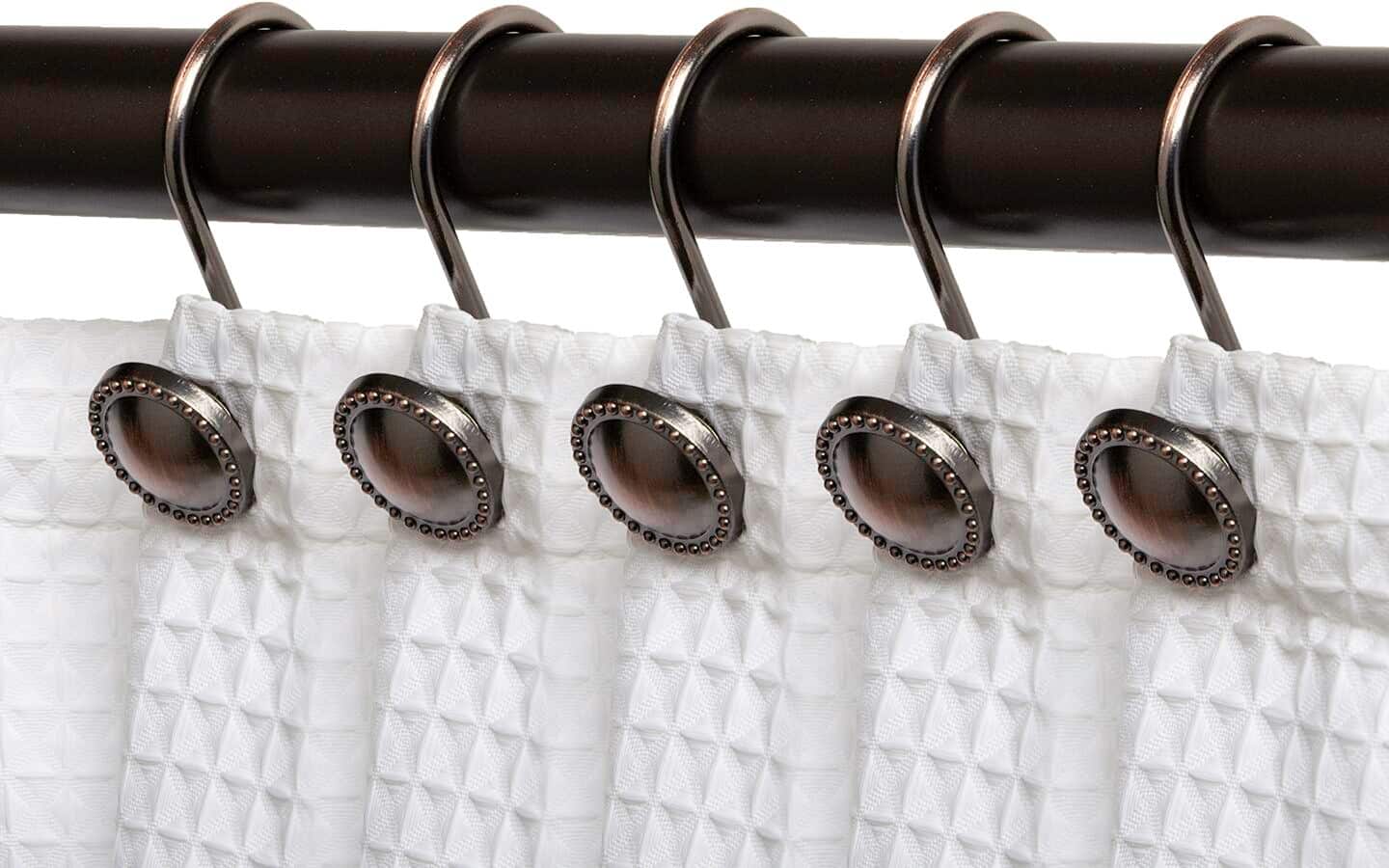 A metal shower curtain rod matching shower curtain hooks holding a white curtain.