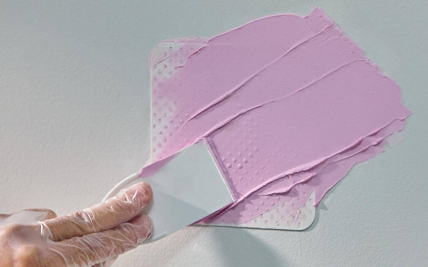 A person applies pink joint compound to wall during drywall repair. A person applies pink joint compound to wall during drywall repair.