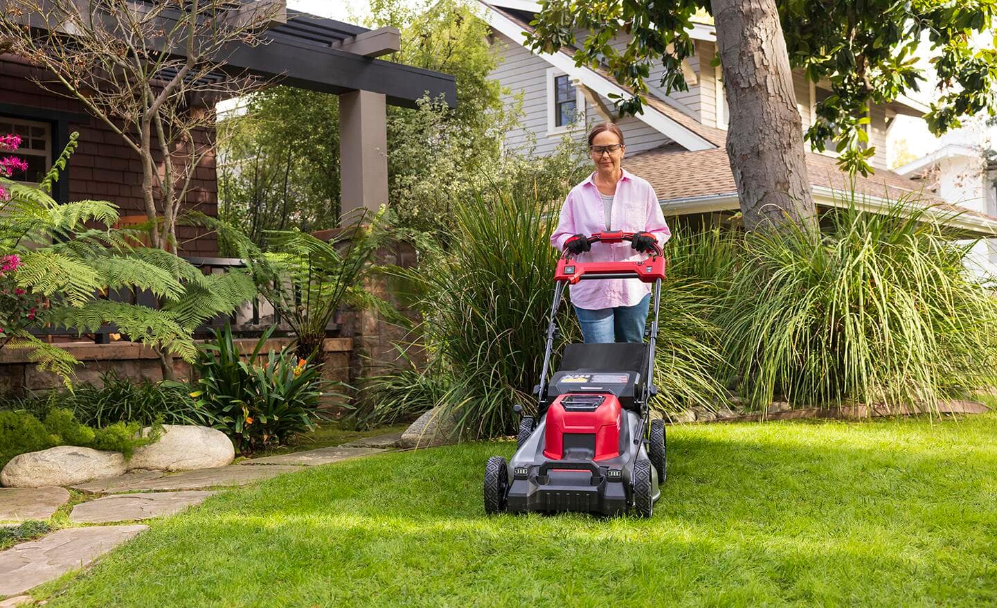 Person pushes a lawnmower in a home landscape