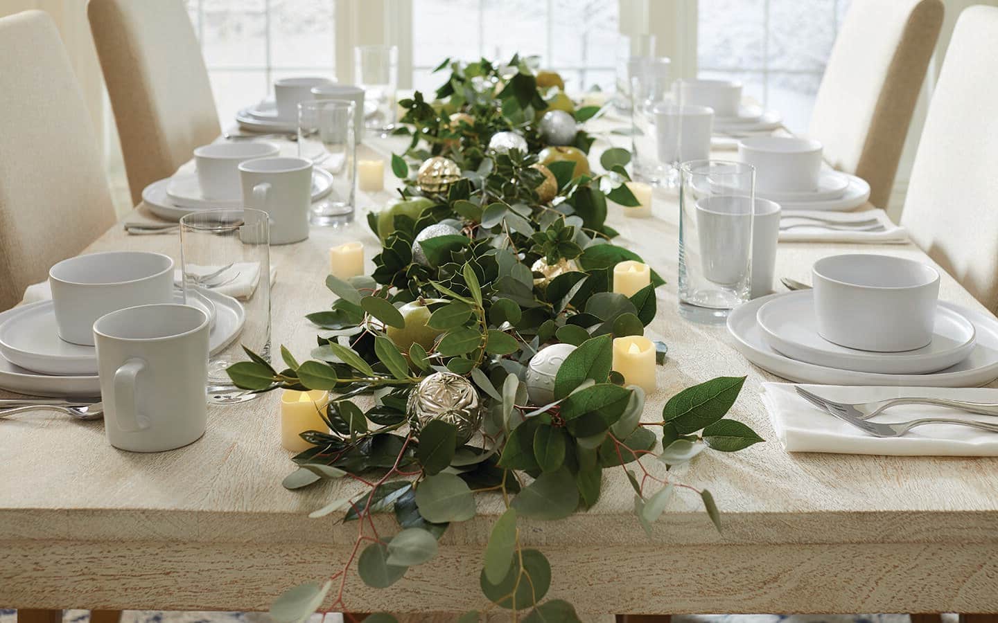 A table-long centerpiece made from different types of fresh greenery and Christmas ornaments.