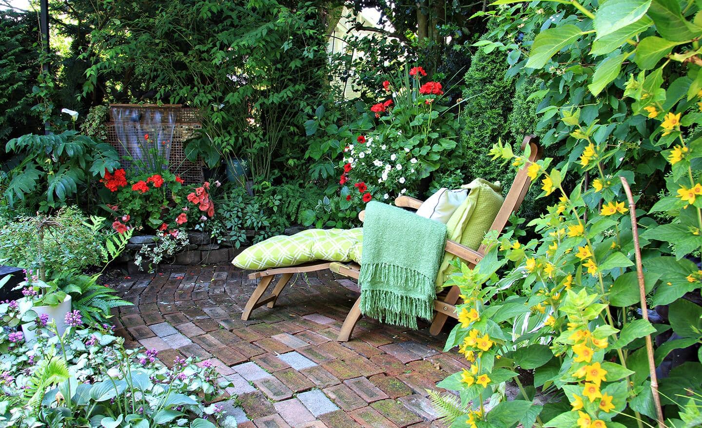 A chaise lounge chair on a patio surrounded by garden plants and flowers