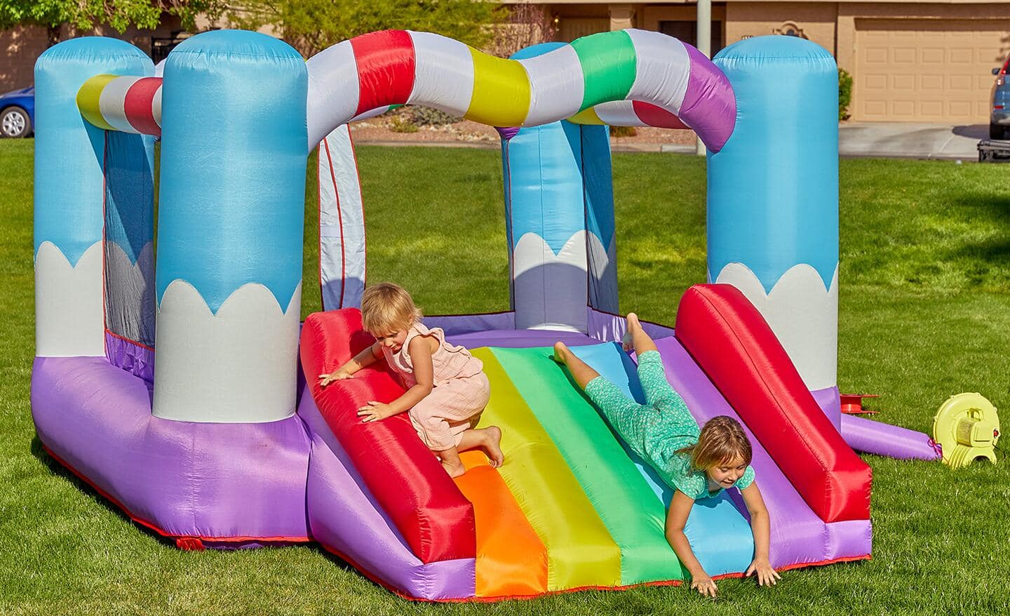 Two children playing on an inflatable, multicolored bounce house.