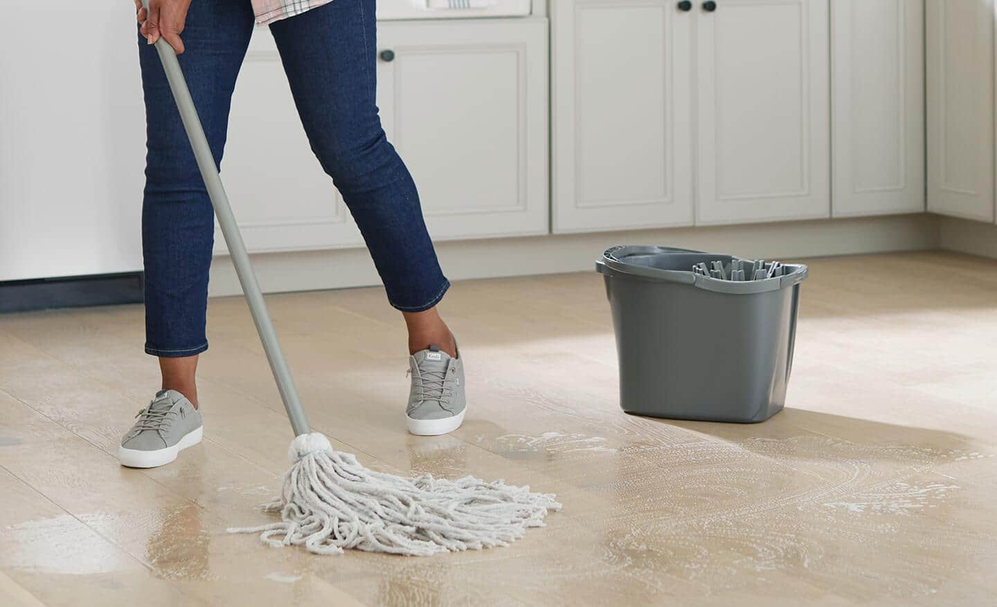 A person using a string mop to clean a kitchen floor.