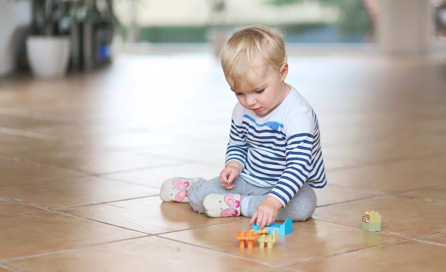 A toddler sits on a tile floor and plays with toys.