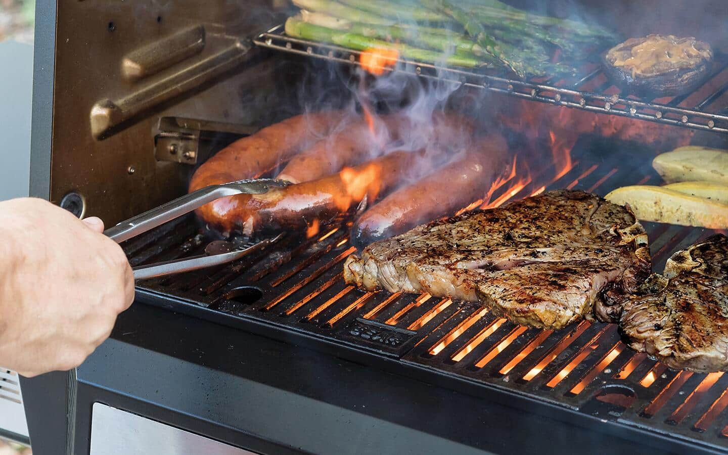 A person cooks meats and vegetables on a barbecue grill. A person cooks meats and vegetables on a barbecue grill.