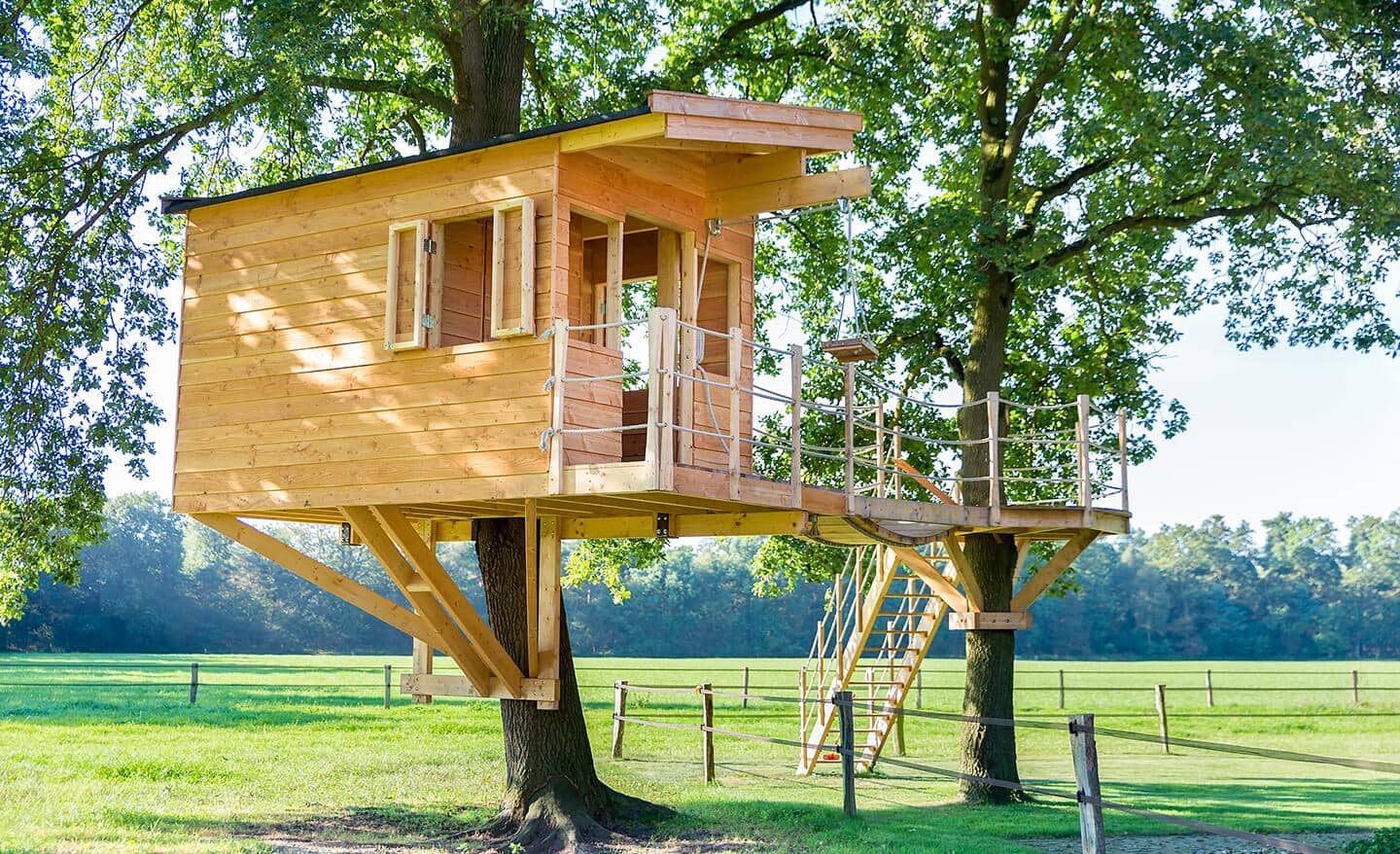 A wood treehouse built in a backyard supported by two trees.