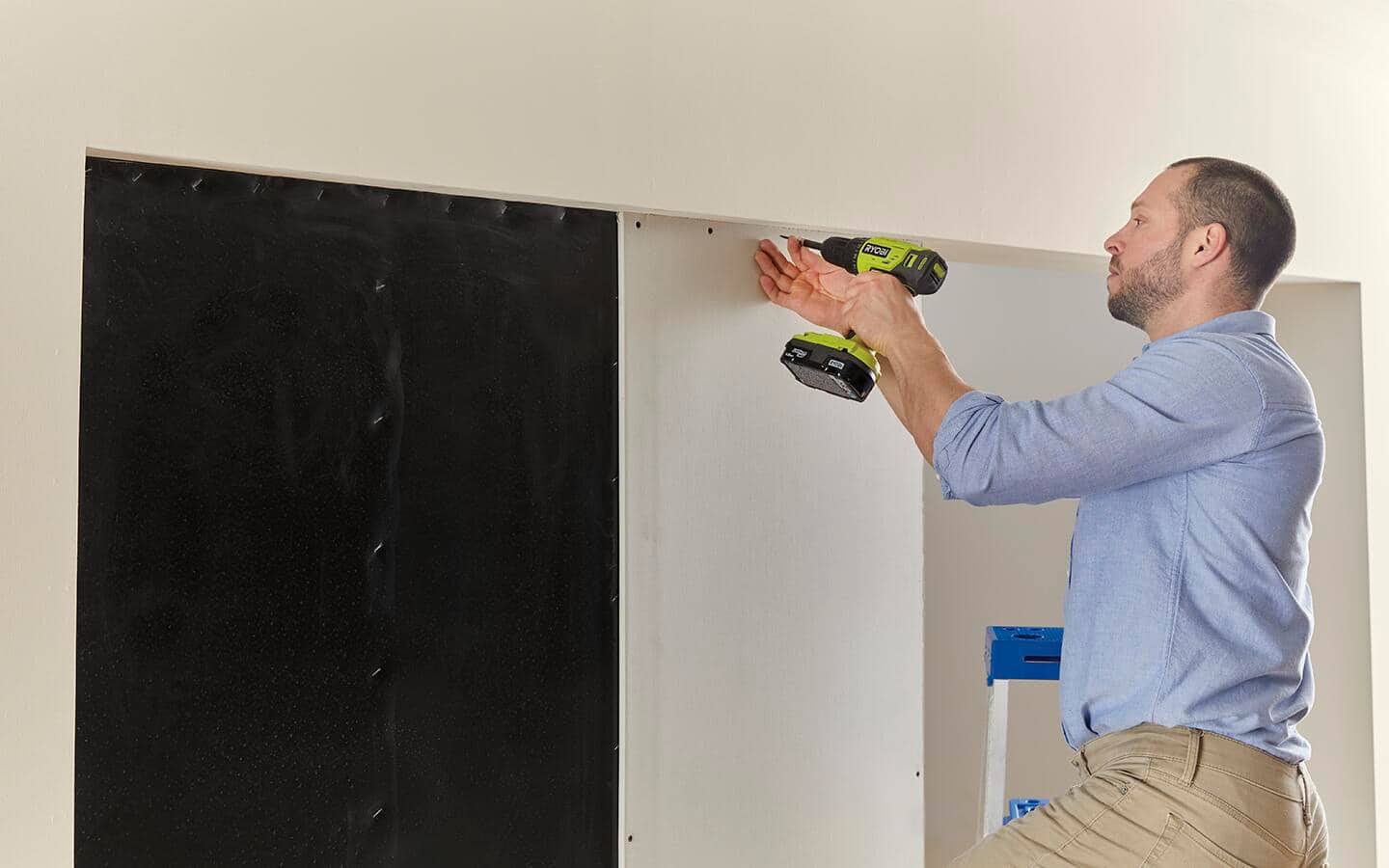 A man using a cordless drill to install sound proofing in a wall.