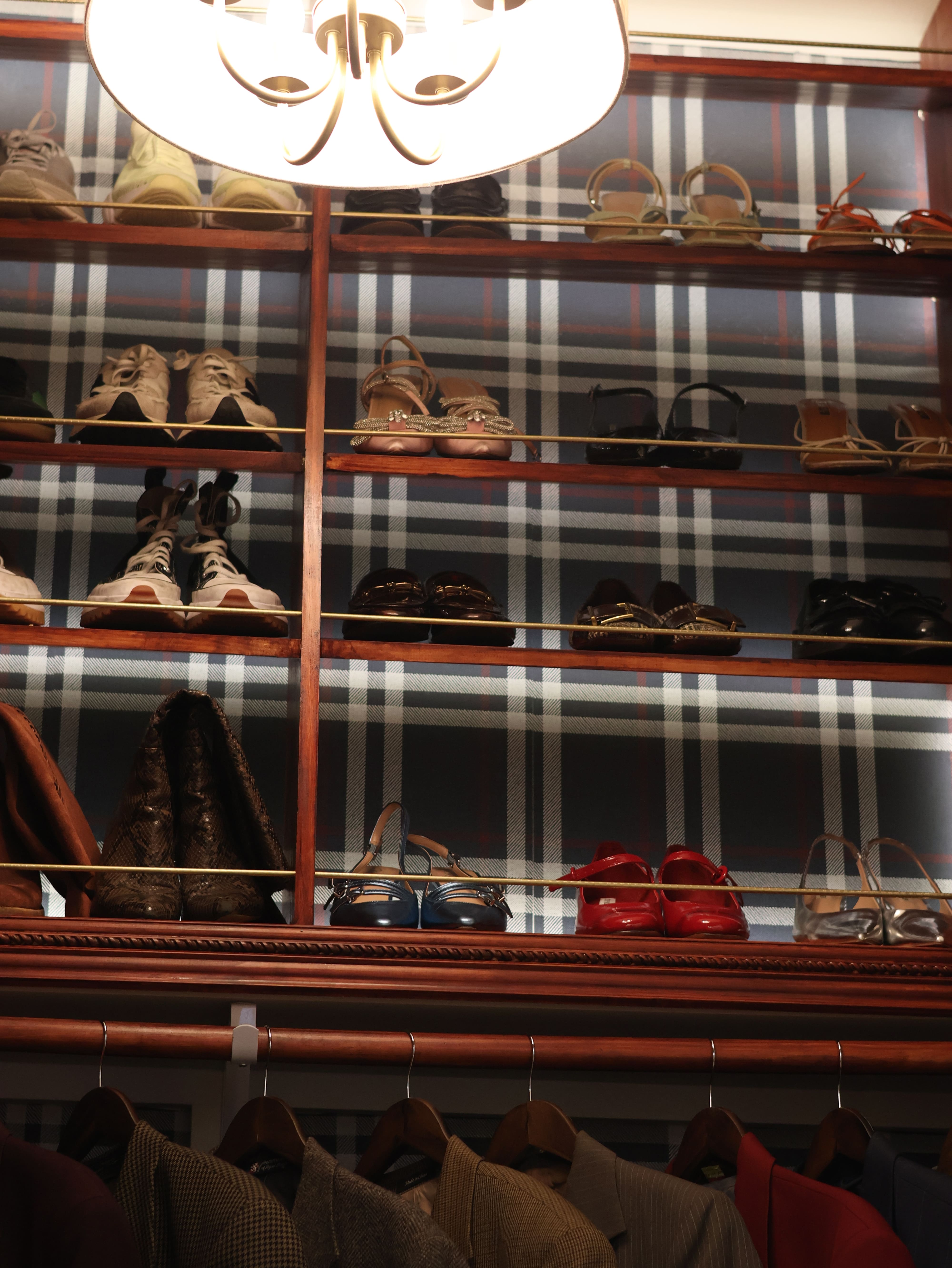 A beautifully designed closet space featuring wooden accents, shelves for shoe storage, thoughtful ambient lighting, and plaid wallpaper for a luxe feel.  