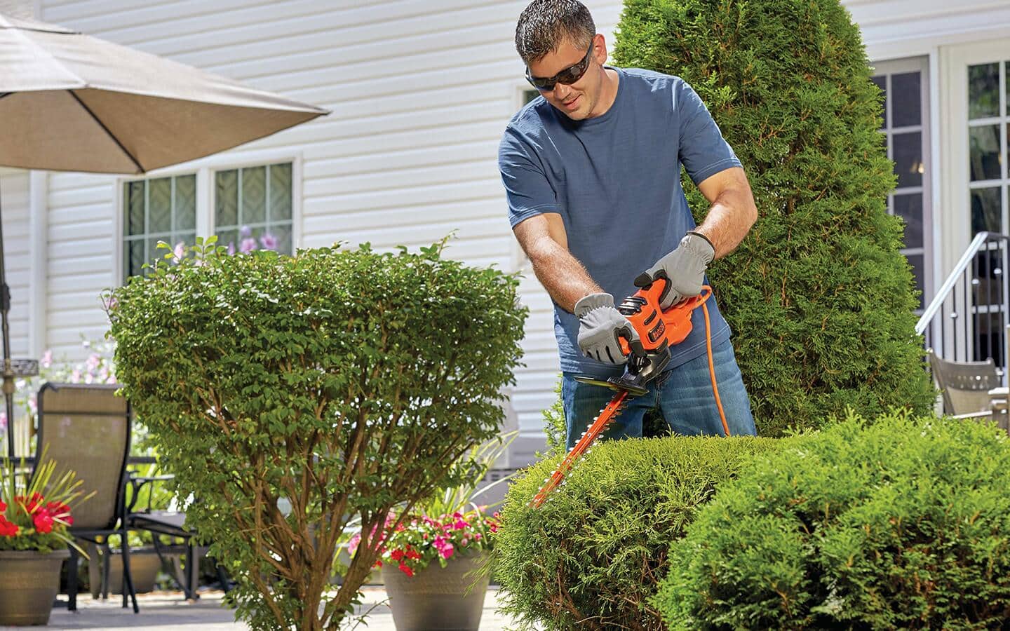 A homeowner uses a hedge trimmer to landscape a yard. A homeowner uses a hedge trimmer to landscape a yard.