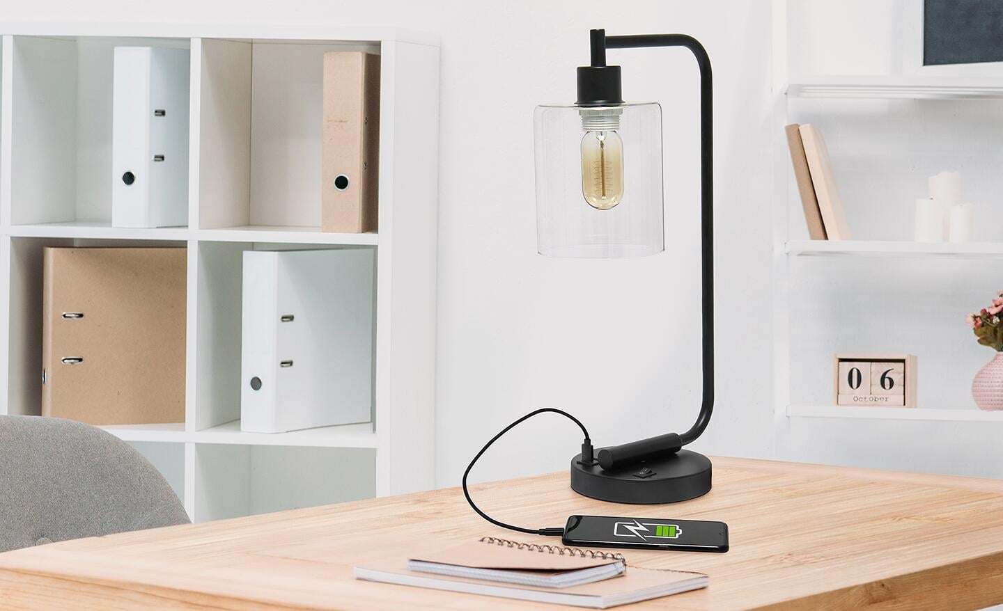 A desk lamp with a USB outlet that is connected to and charging a smartphone.