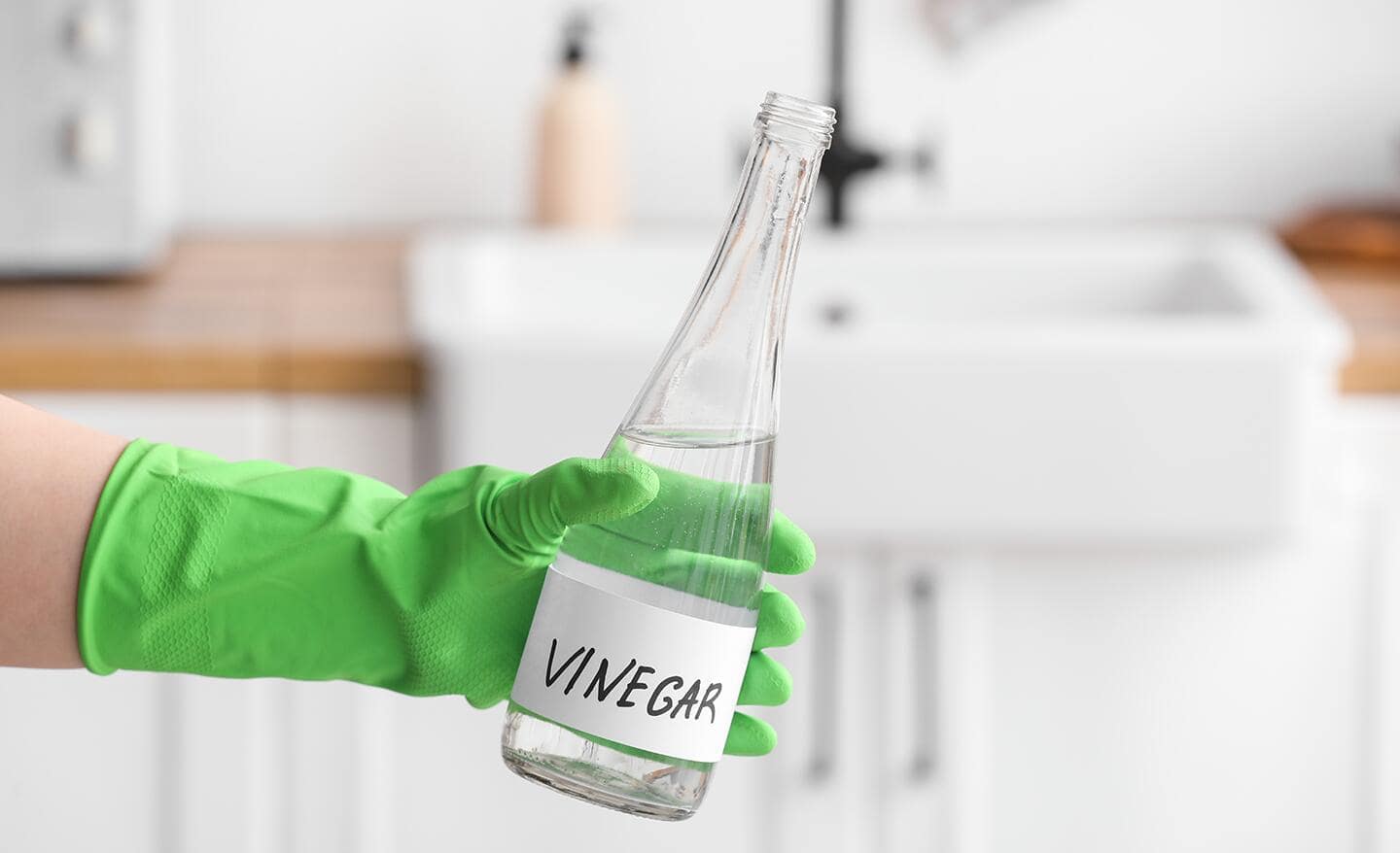 Someone wearing cleaning gloves and holding a glass bottle of vinegar.