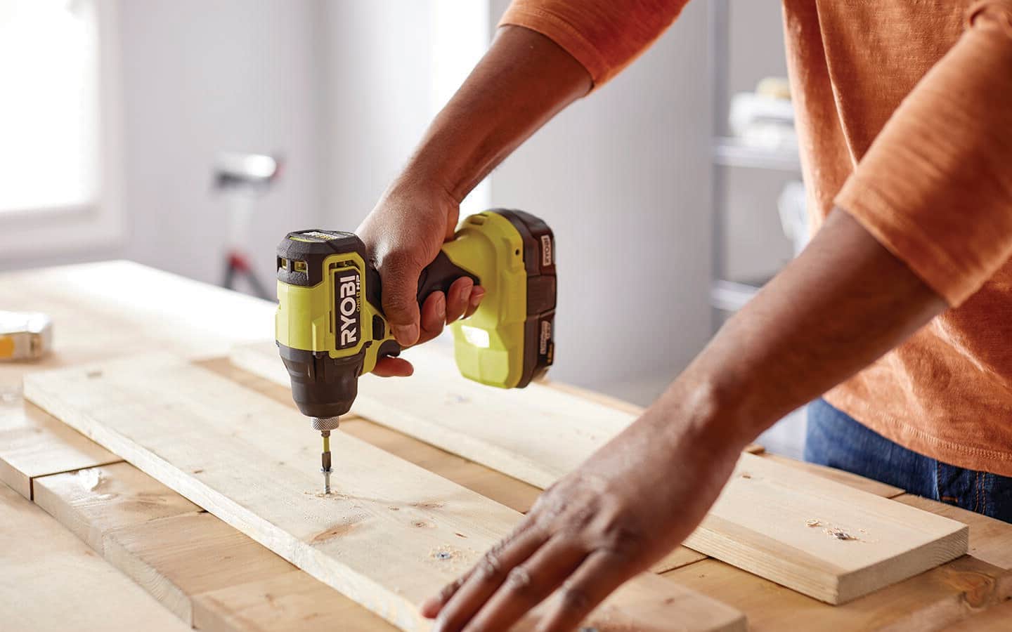 Someone using a cordless drill to attach a wooden board to a craft board.