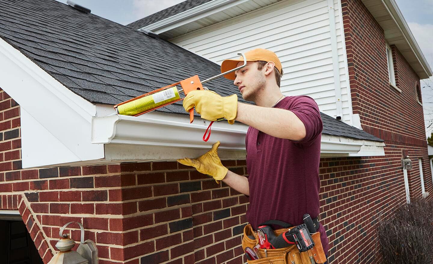 A person applying silicone to seal part of a gutter system.