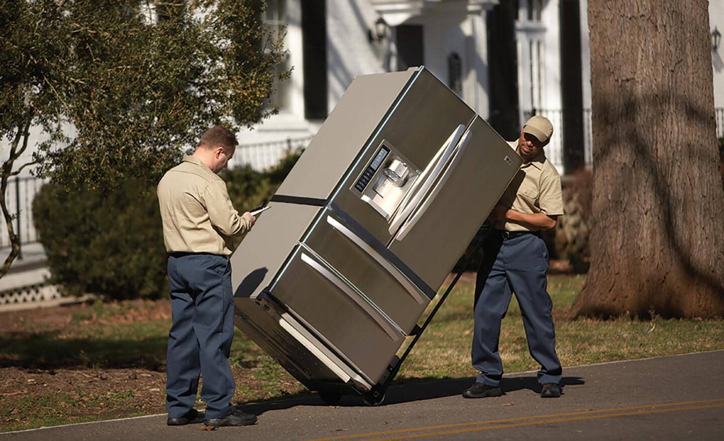 Two delivery men transporting a french door refrigerator on a dolly.