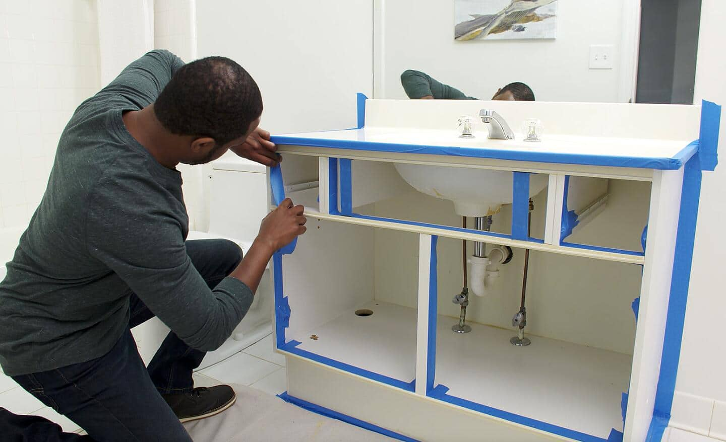 A person applying painter's tape to the edges of bath vanity to be painted.