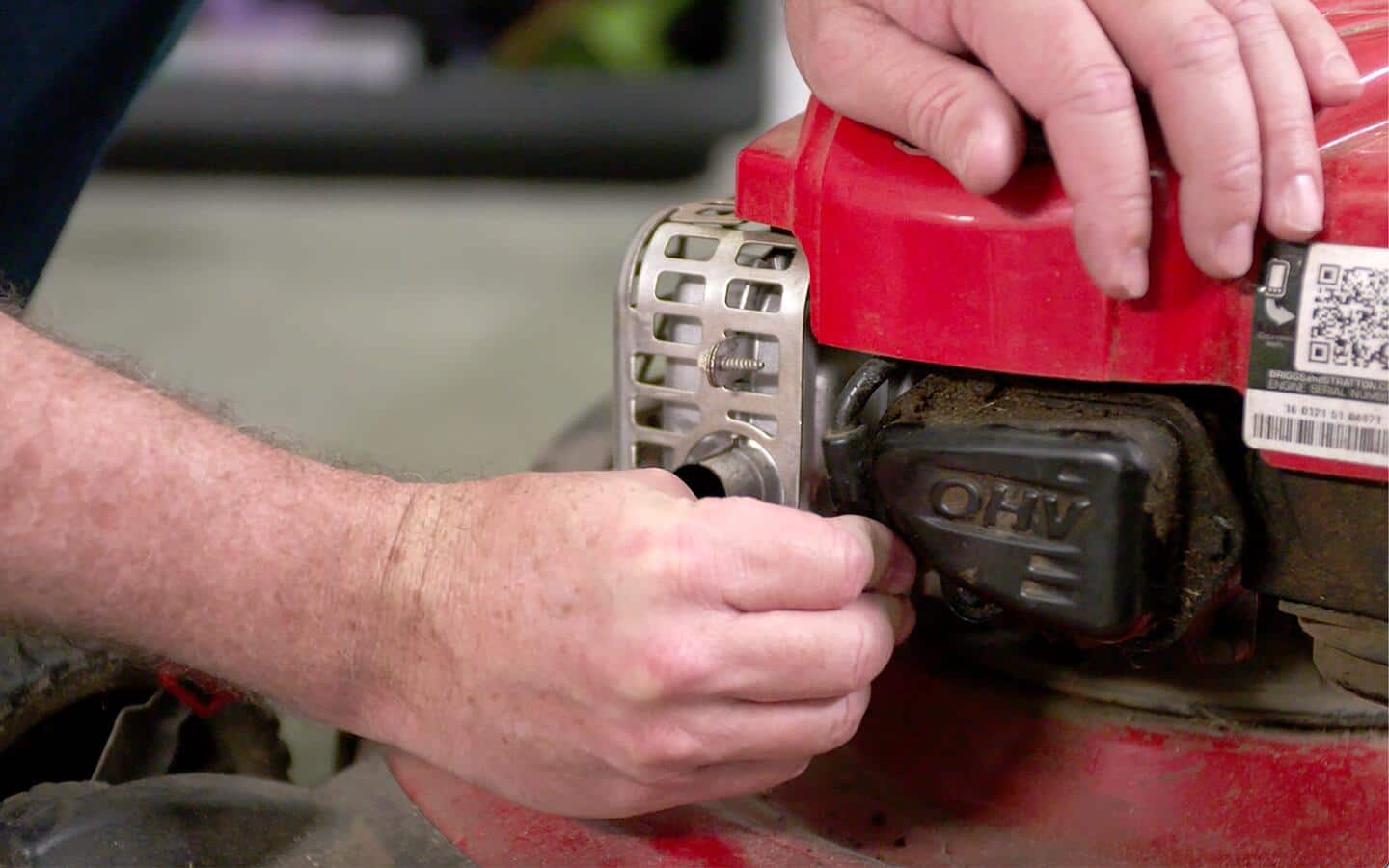 Someone changes a lawn mower's spark plug. Someone changes a lawn mower's spark plug.