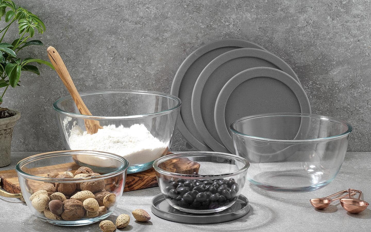 Glass mixing bowls filled with flour, nuts and more sitting on a counter.