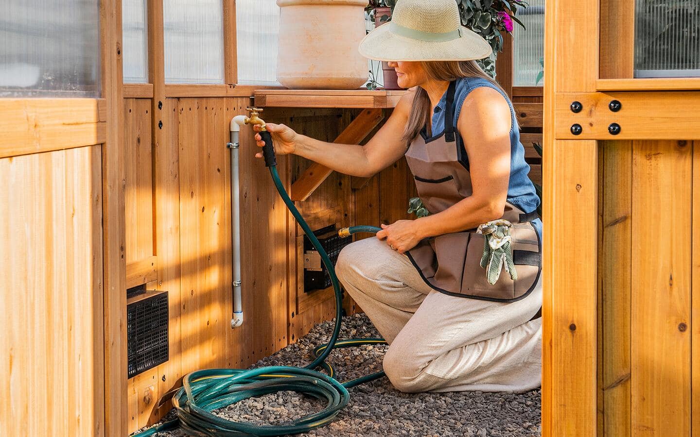 A person secures a garden hose to a faucet in a greenhouse