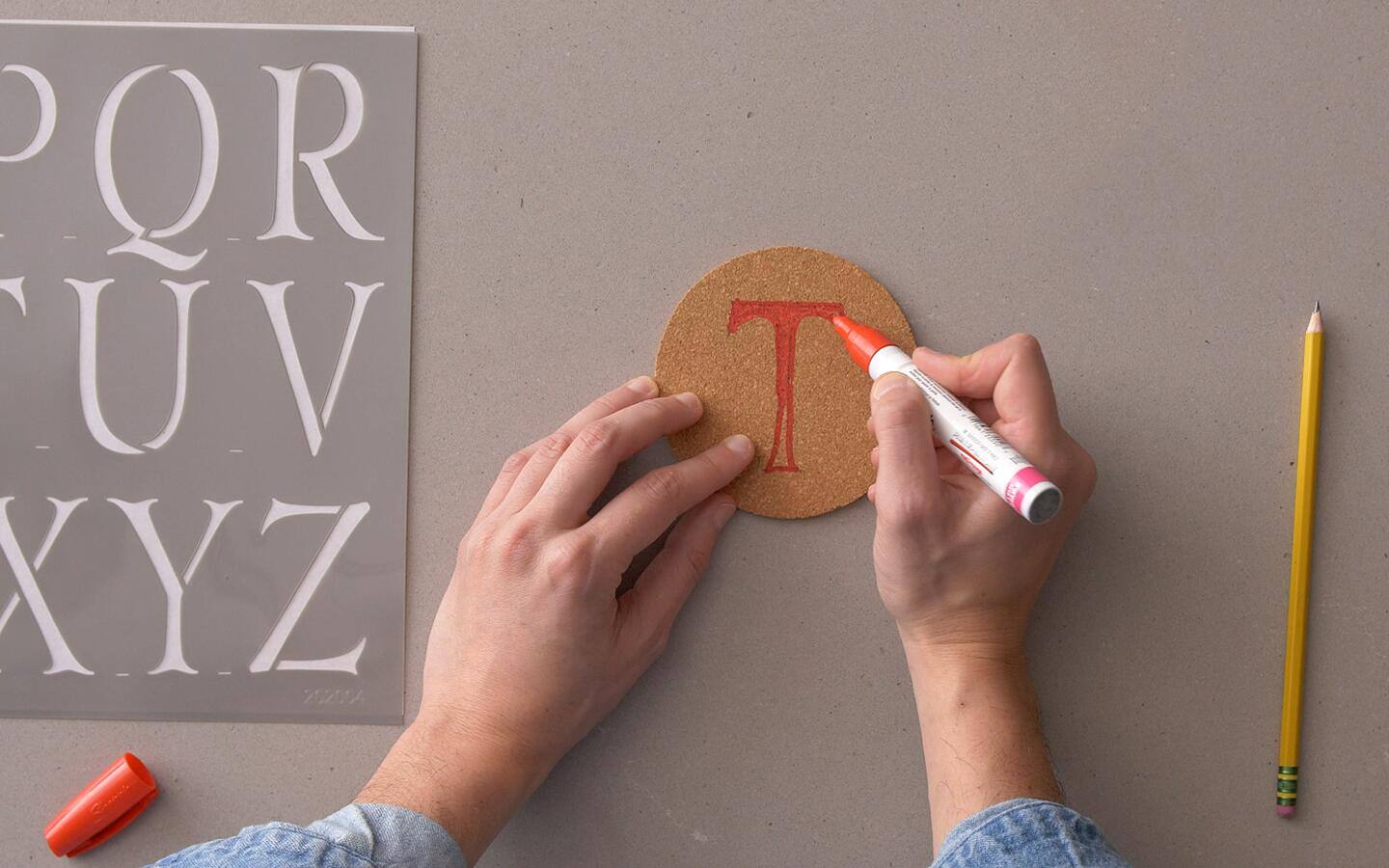 A letter "T" is written on a coaster and colored with a red marker. 
