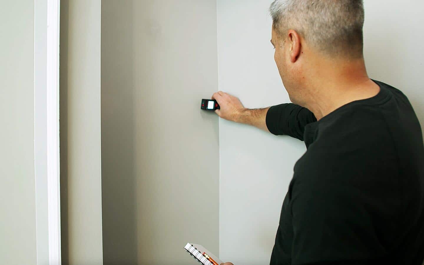 A man using a laser to measure a closet wall.