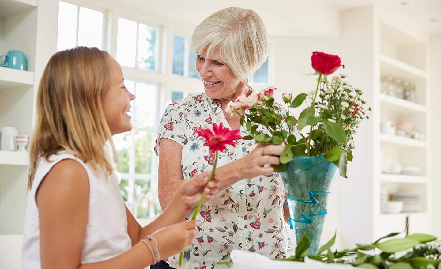 A woman and girl arranging cut roses in a vase