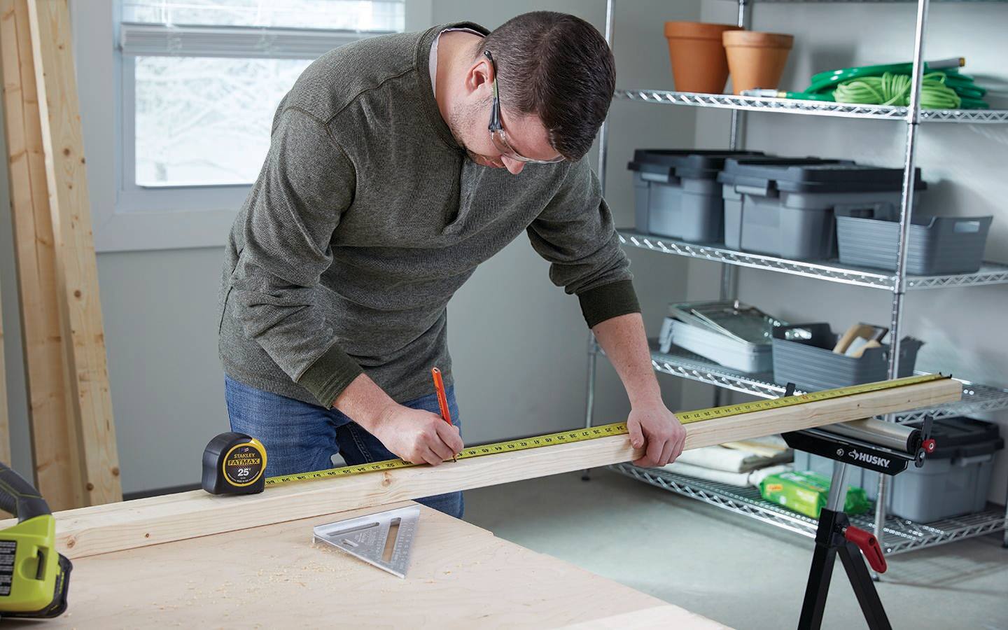 A man in a workshop uses a measuring tape and a pencil to mark where a board should be cut. A man in a workshop uses a measuring tape and a pencil to mark where a board should be cut.