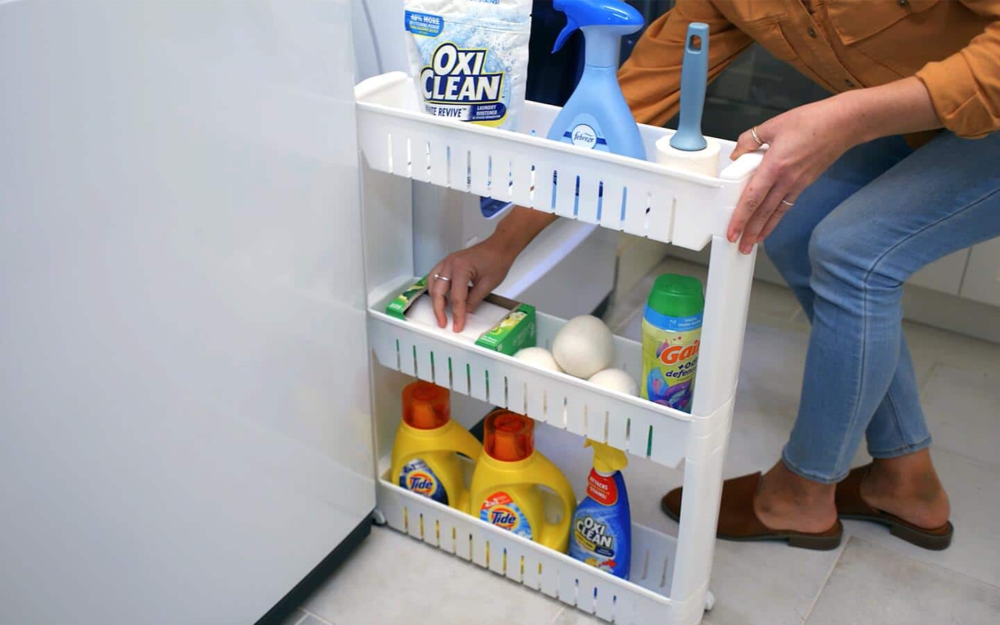 Someone using a pull-out caddy stocked with laundry supplies. Someone using a pull-out caddy stocked with laundry supplies.