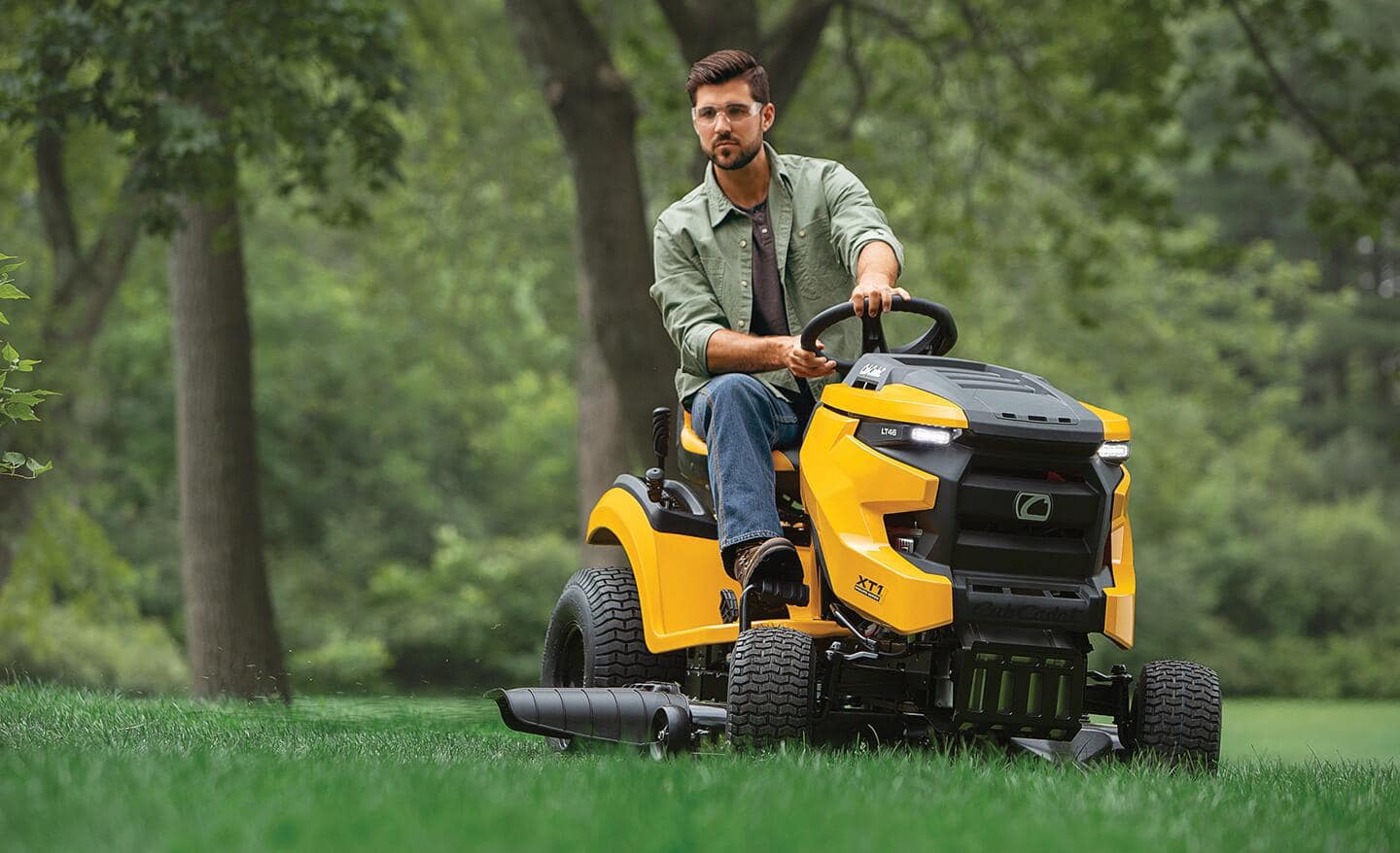 A man in a green shirt riding on a yellow lawn mower. 