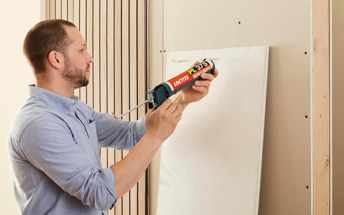A man applying glue adhesive to wood paneling for a room divider wall.