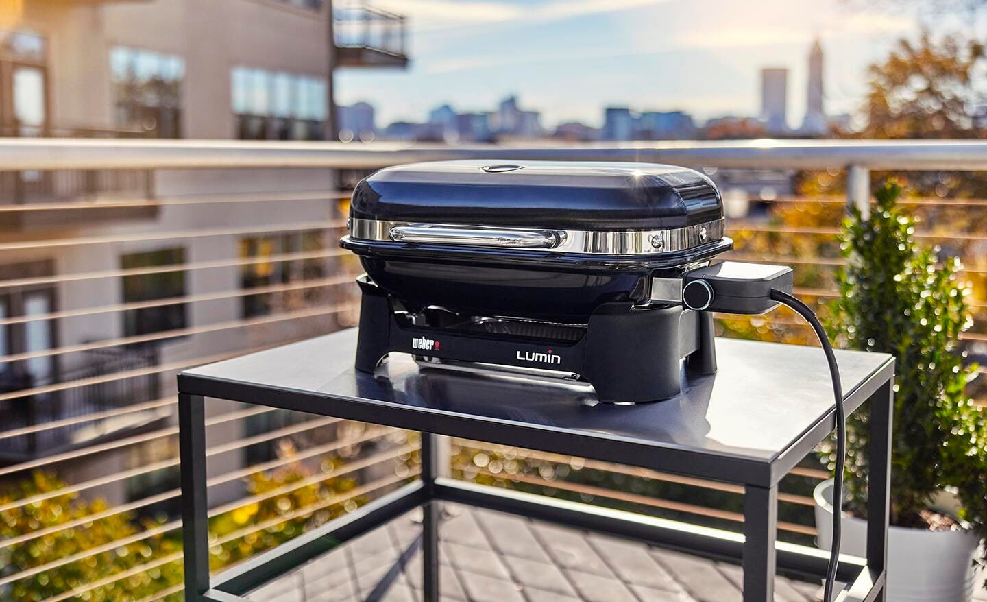An electric grill sits on a table on a balcony with a city view.