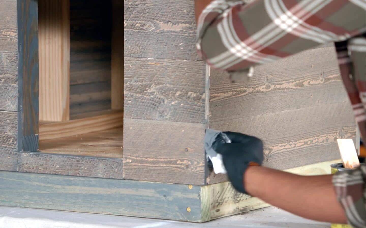 A person in gloves touching up the wood on a dog house.