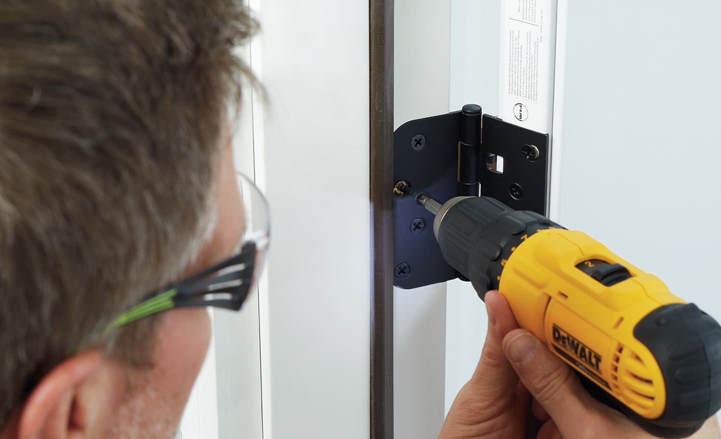 A man drilling hinges into a new entry door inside the home.