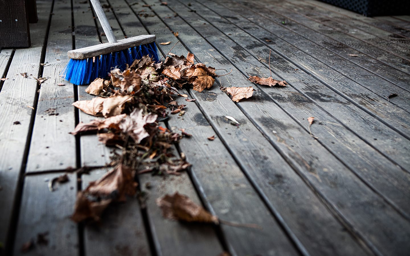 A broom with leaves and debris on a wood deck 